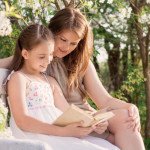 Happy mother with daughter with book in spring garden