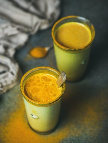 Golden turmeric milk with turmeric powder on edges of glass