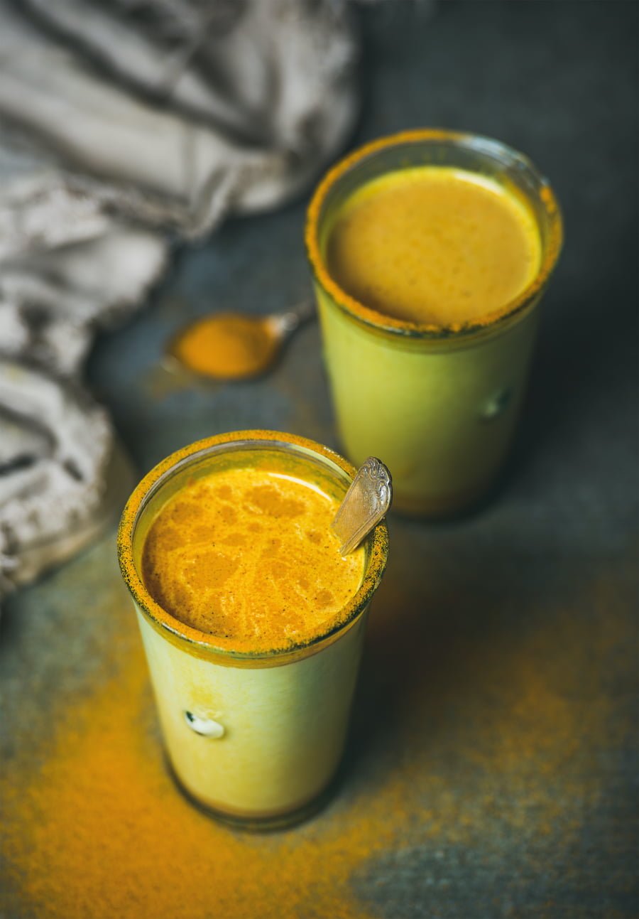 Golden turmeric milk with turmeric powder on edges of glass