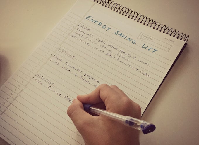 Child's hand writing out an energy saving checklist for the home