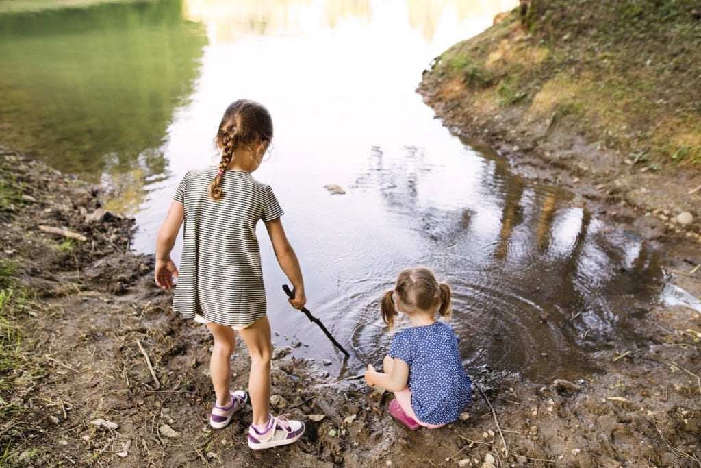 Young girls spending time in nature playing at the edge of a lake