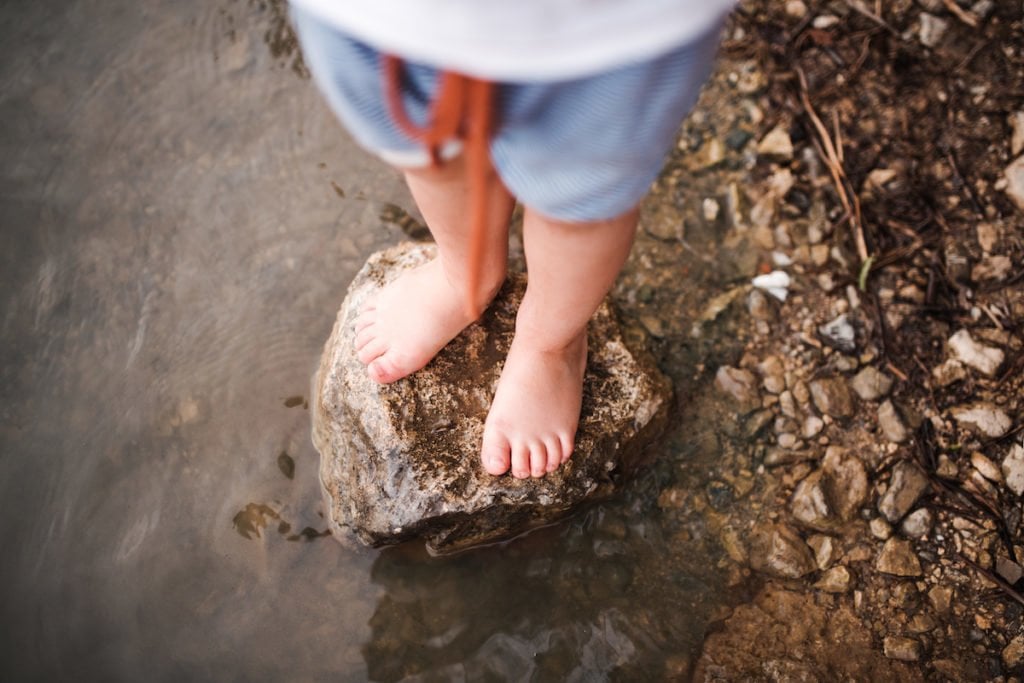 Child playing outside in nature with bare feet near the water