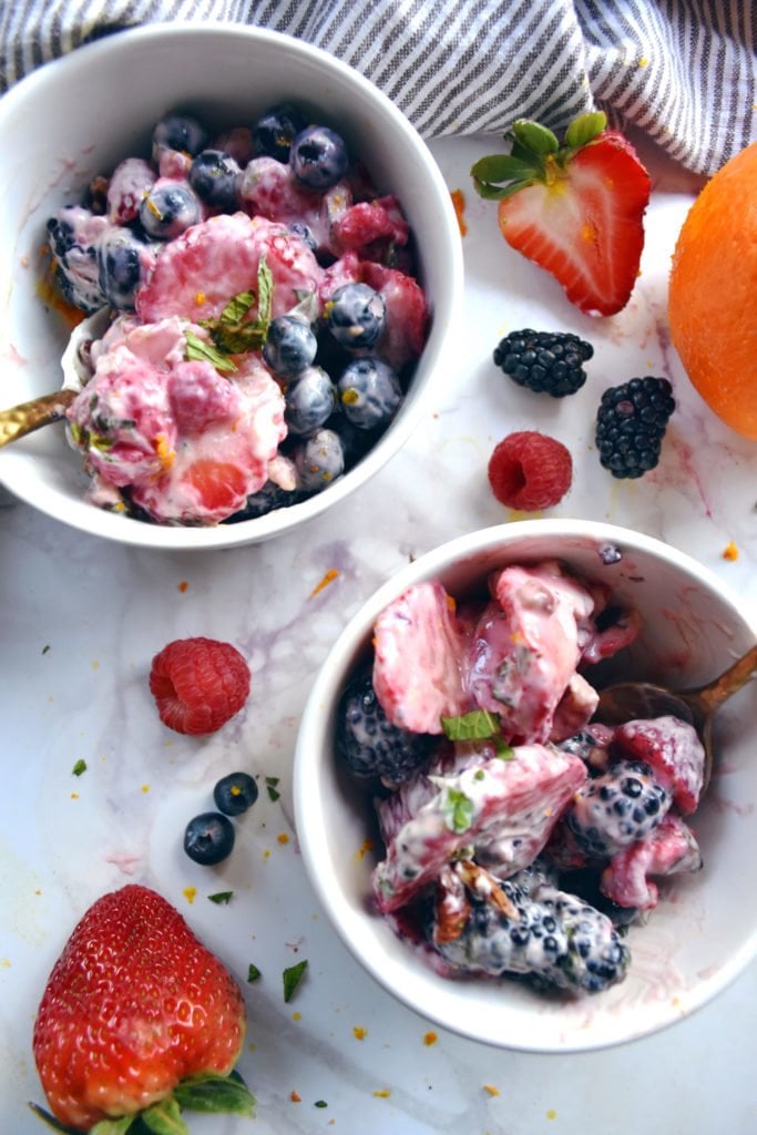 Fresh berry fruit salad with yogurt in bowls with fruit on white marble counter