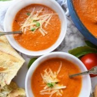 Roasted tomato and basil soup in two bowls next to dutch oven