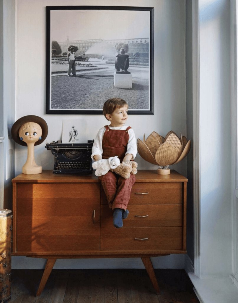 Child sitting on midcentury modern dresser looking out window